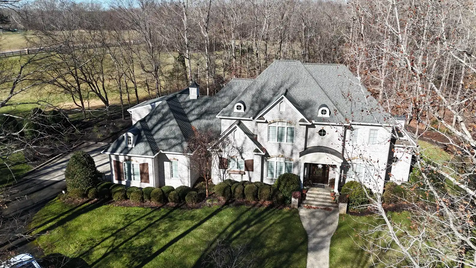 Aerial view of a large brick home in Lewisville, NC with a new GAF Woodland designer shingle roof on a complex hip roof with dormers, in Castlewood Gray