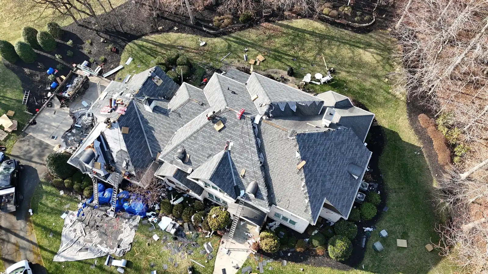 Overhead drone view of a large complex hip roof in Lewisville, NC partway through installation of GAF Woodland Castlewood Gray shingles, with crew ladders and materials around the house
