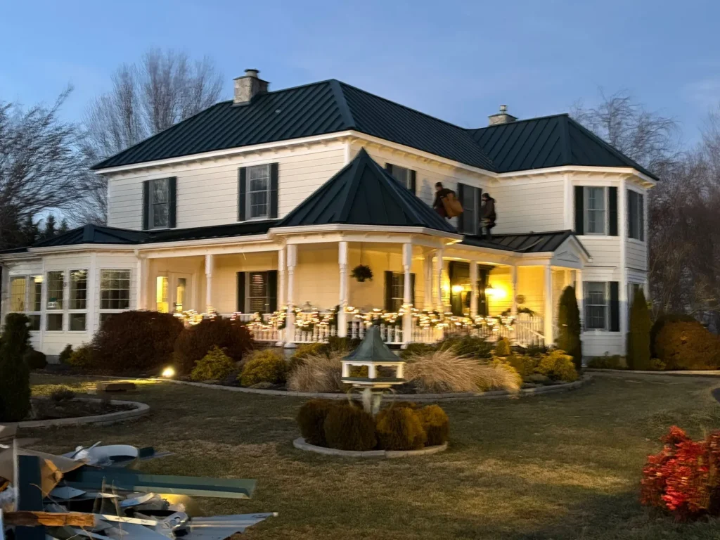 Large white farmhouse in Sparta, NC with a new dark green standing seam metal roof at dusk