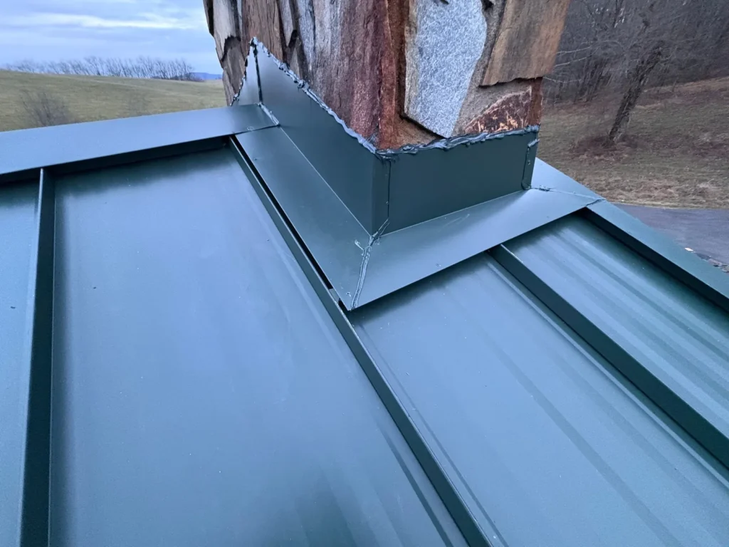 Custom metal chimney flashing on a dark green standing seam metal roof
